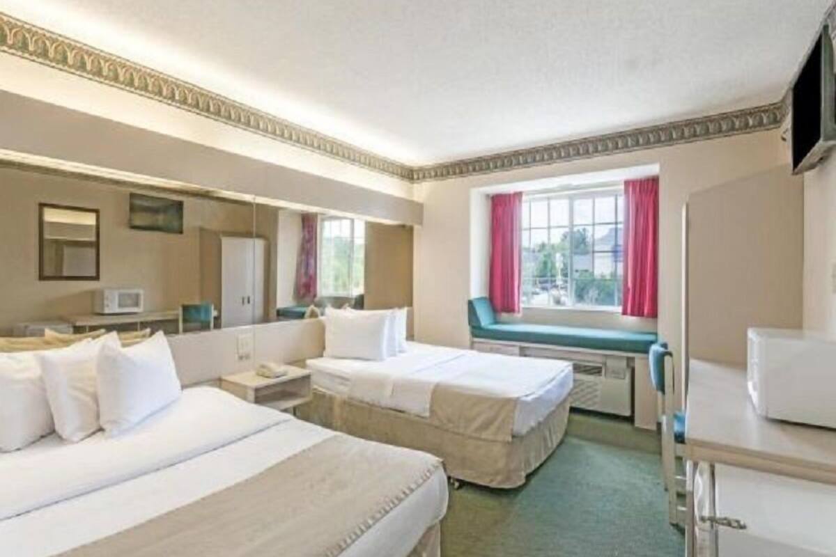 A hotel room with two beds, a desk, a chair, a television, and a window with curtains.