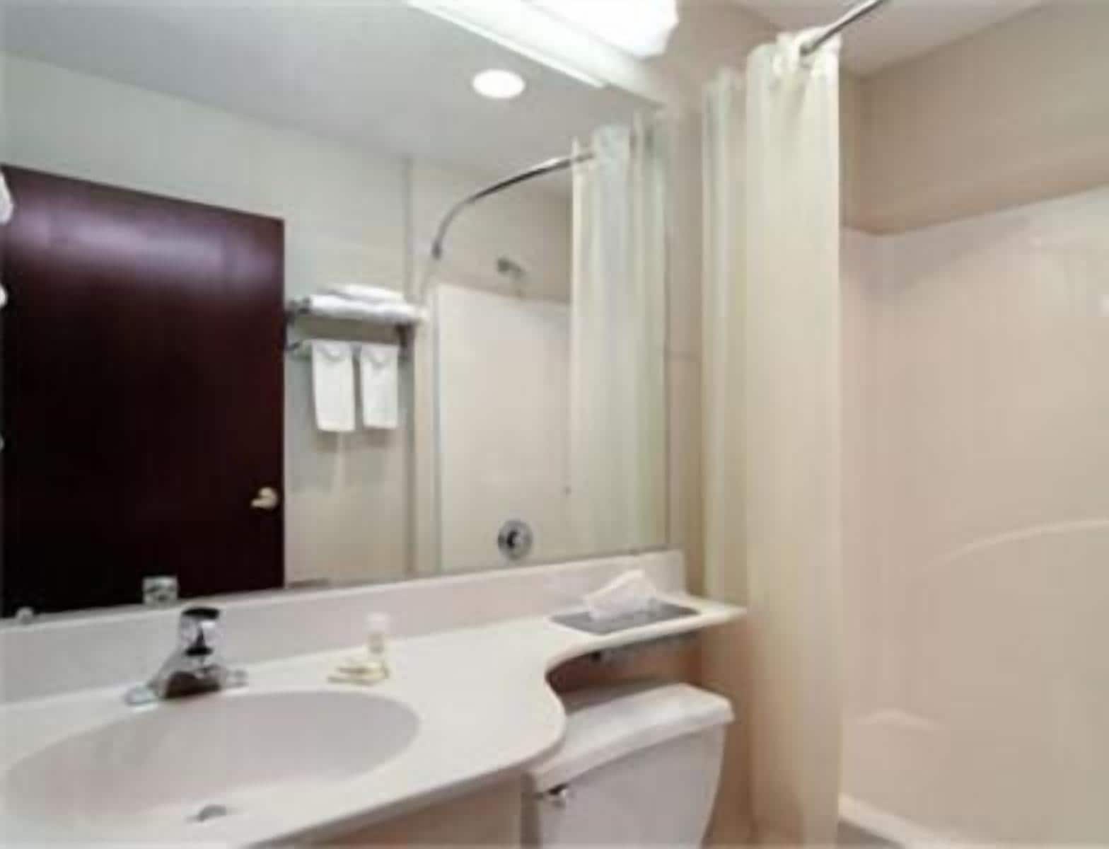 A bathroom with a white sink, a mirror, a dark-colored door, and a shower area.