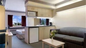 A compact hotel room with a kitchenette, a sofa, a small table, and a window with curtains. - Stay Express Inn & Suites Atlanta (Union City)