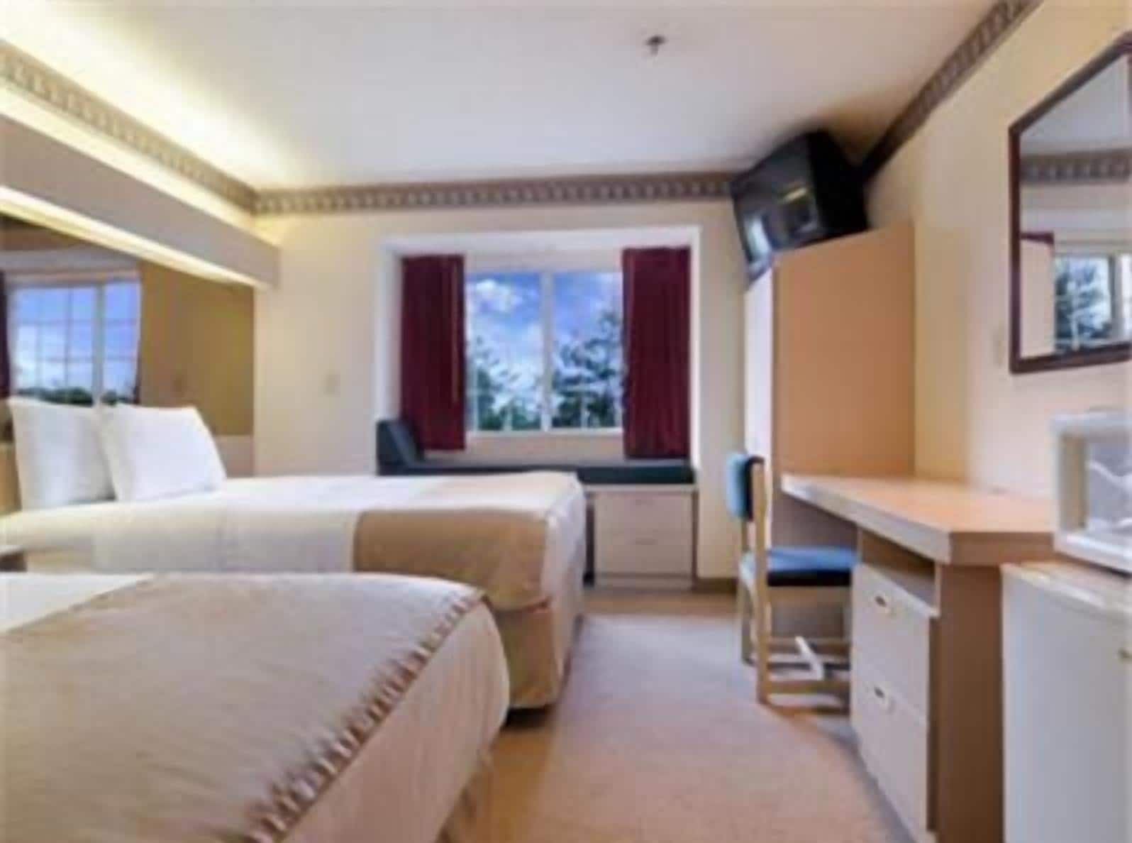 A hotel room with two beds, a desk, a chair, and a TV.