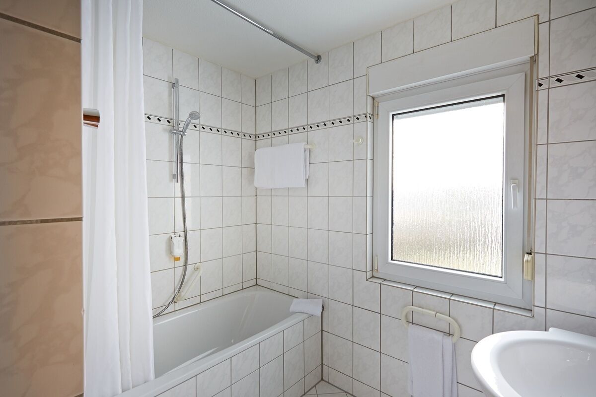 Une salle de bain avec des carreaux blancs, une douche, une baignoire, une fenêtre et un lavabo.