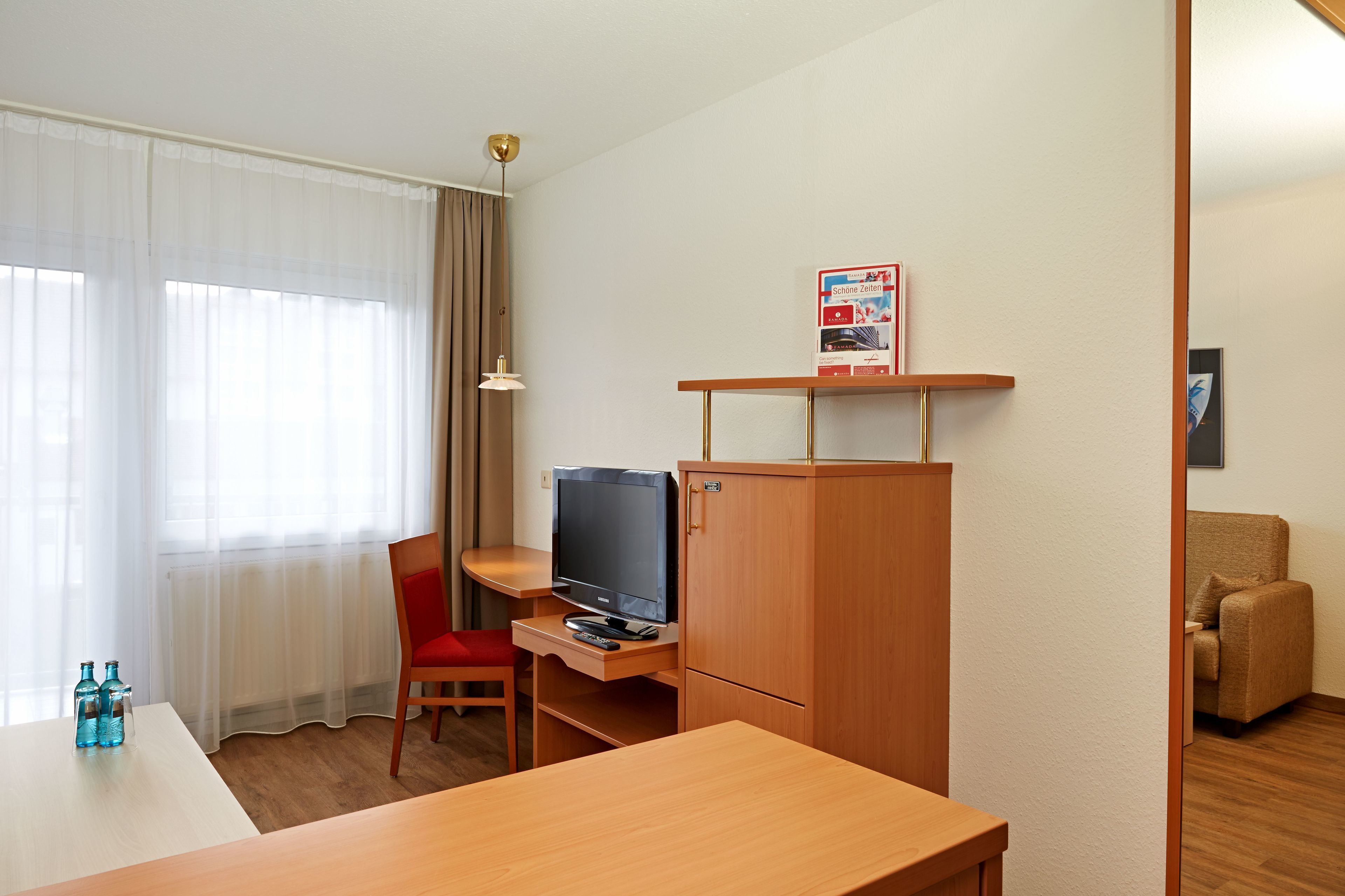 A hotel room with a wooden desk, a television, a chair, and a cabinet.