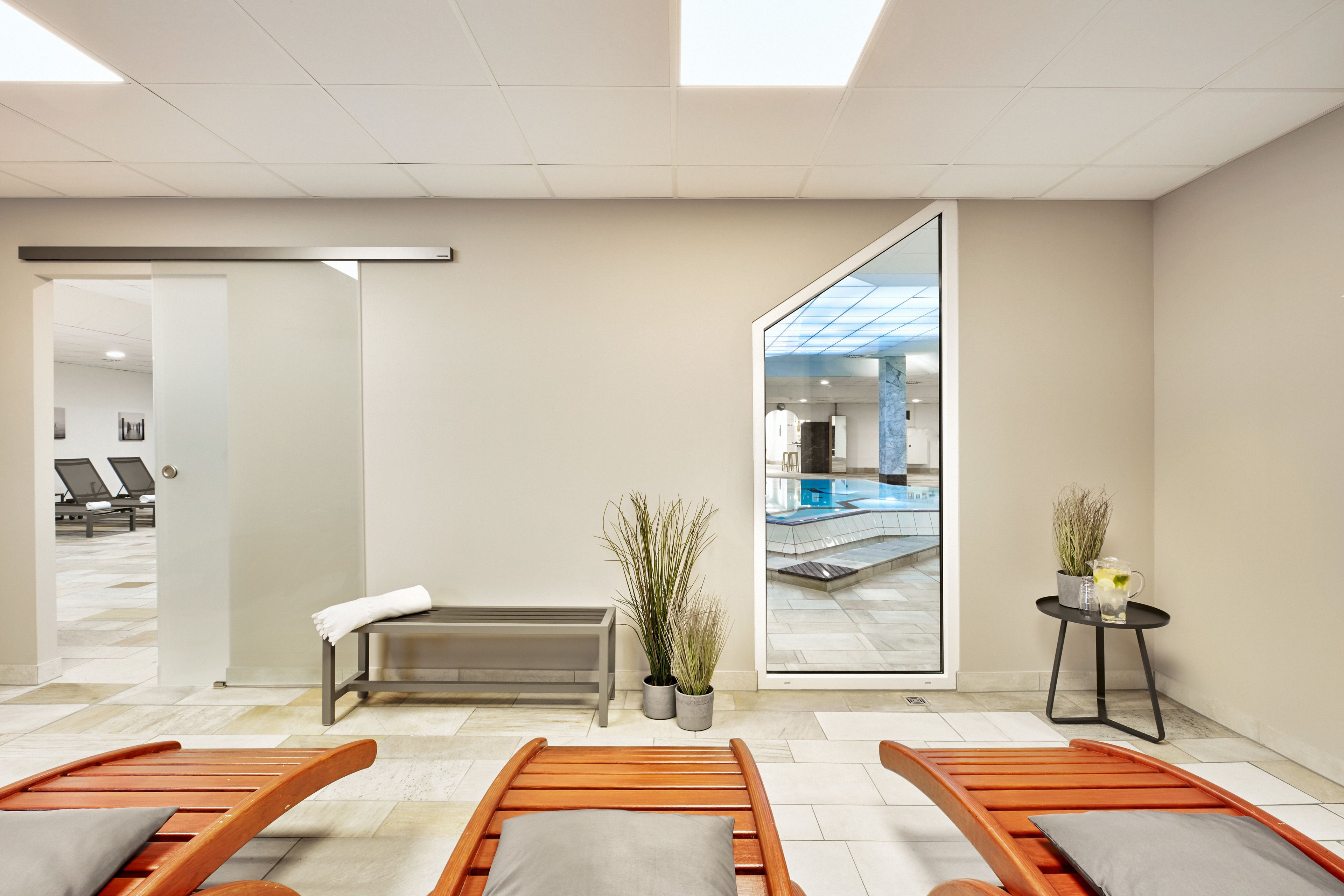 Ein moderner Wellnessraum mit Holzliegen, einer Bank und topfpflanzengepflanzten Pflanzen.