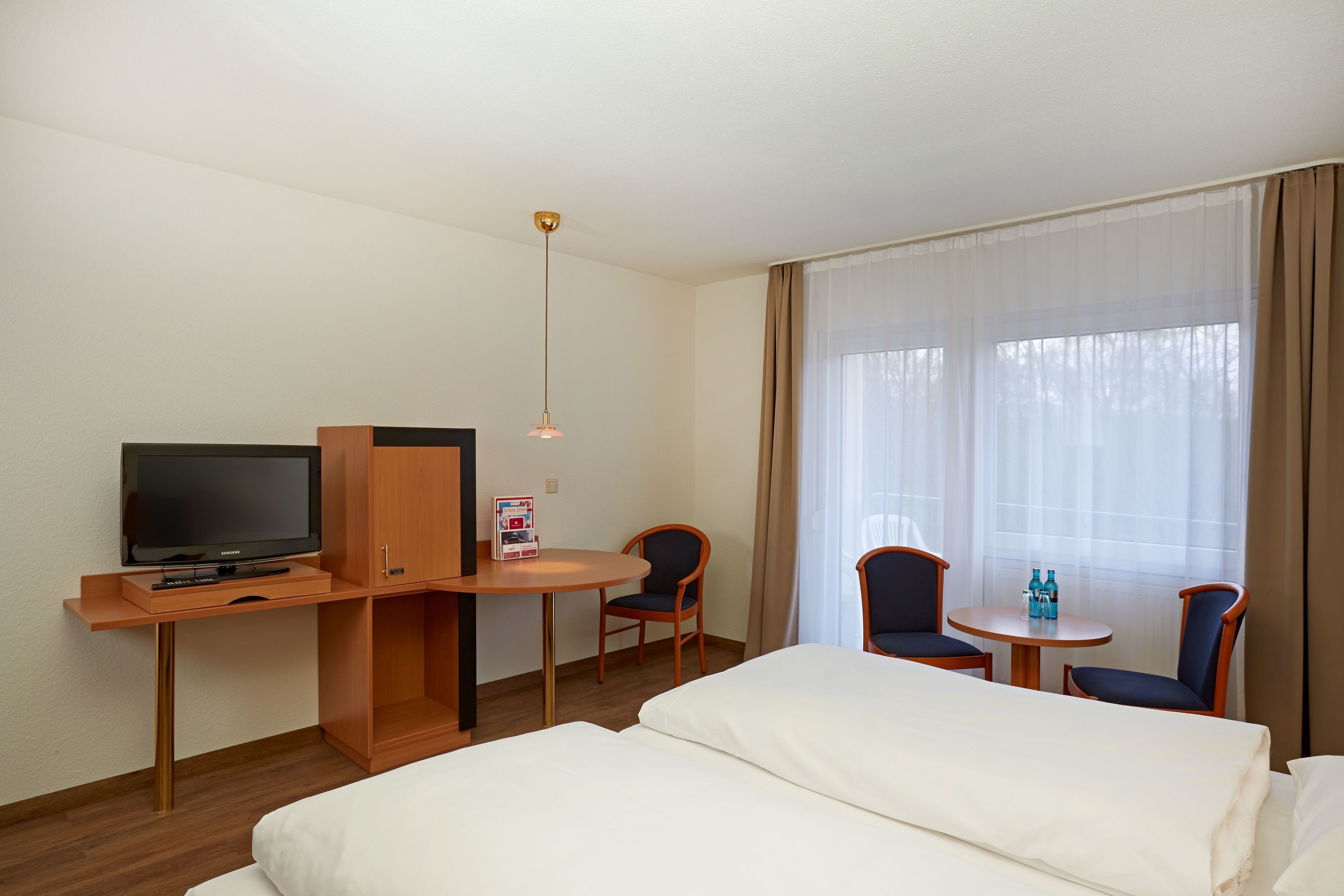 Una camera d'albergo con un letto, una televisione, una scrivania con una sedia e un tavolino con due sedie.