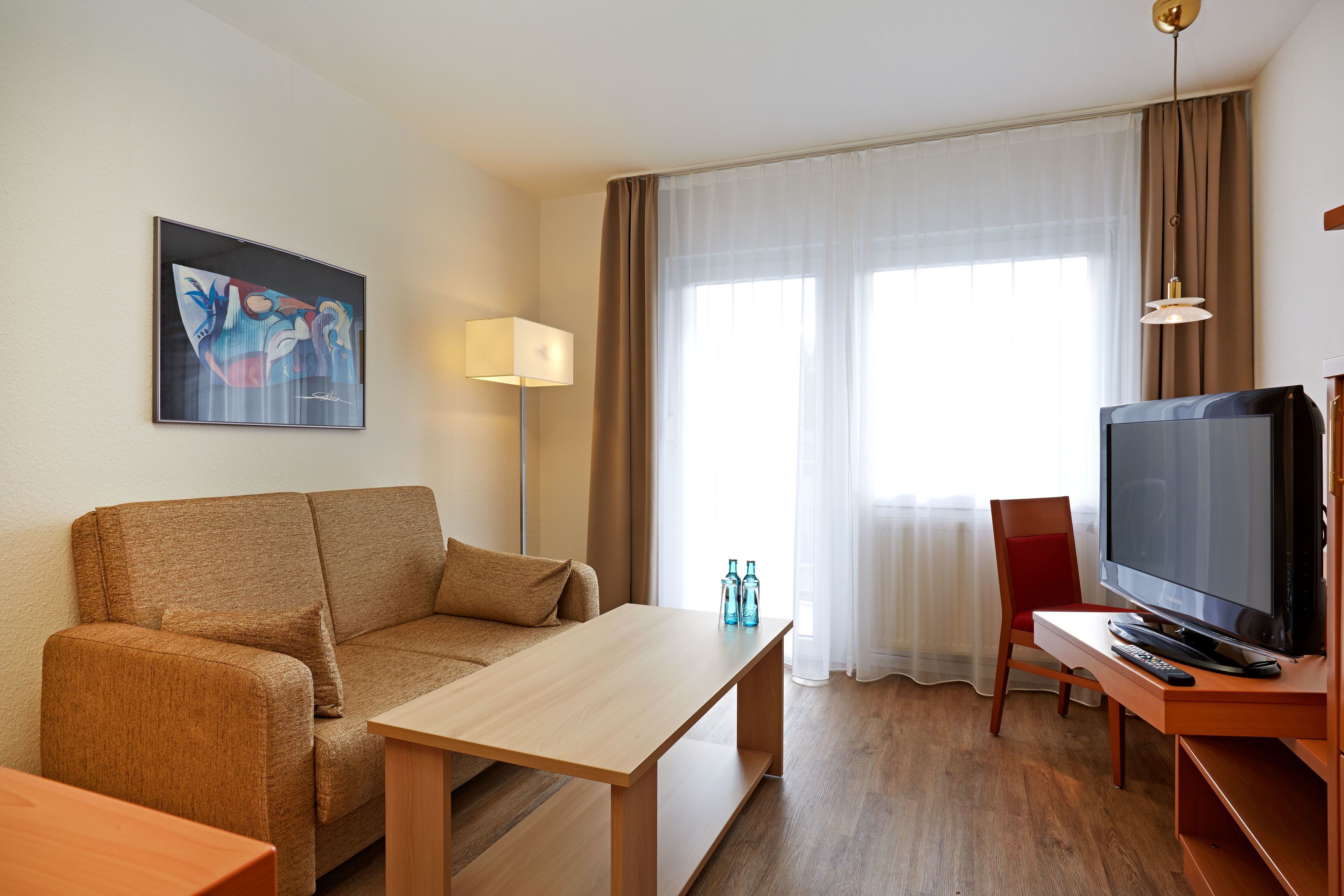 A hotel room with a sofa, a wooden table, a TV, and a painting on the wall.
