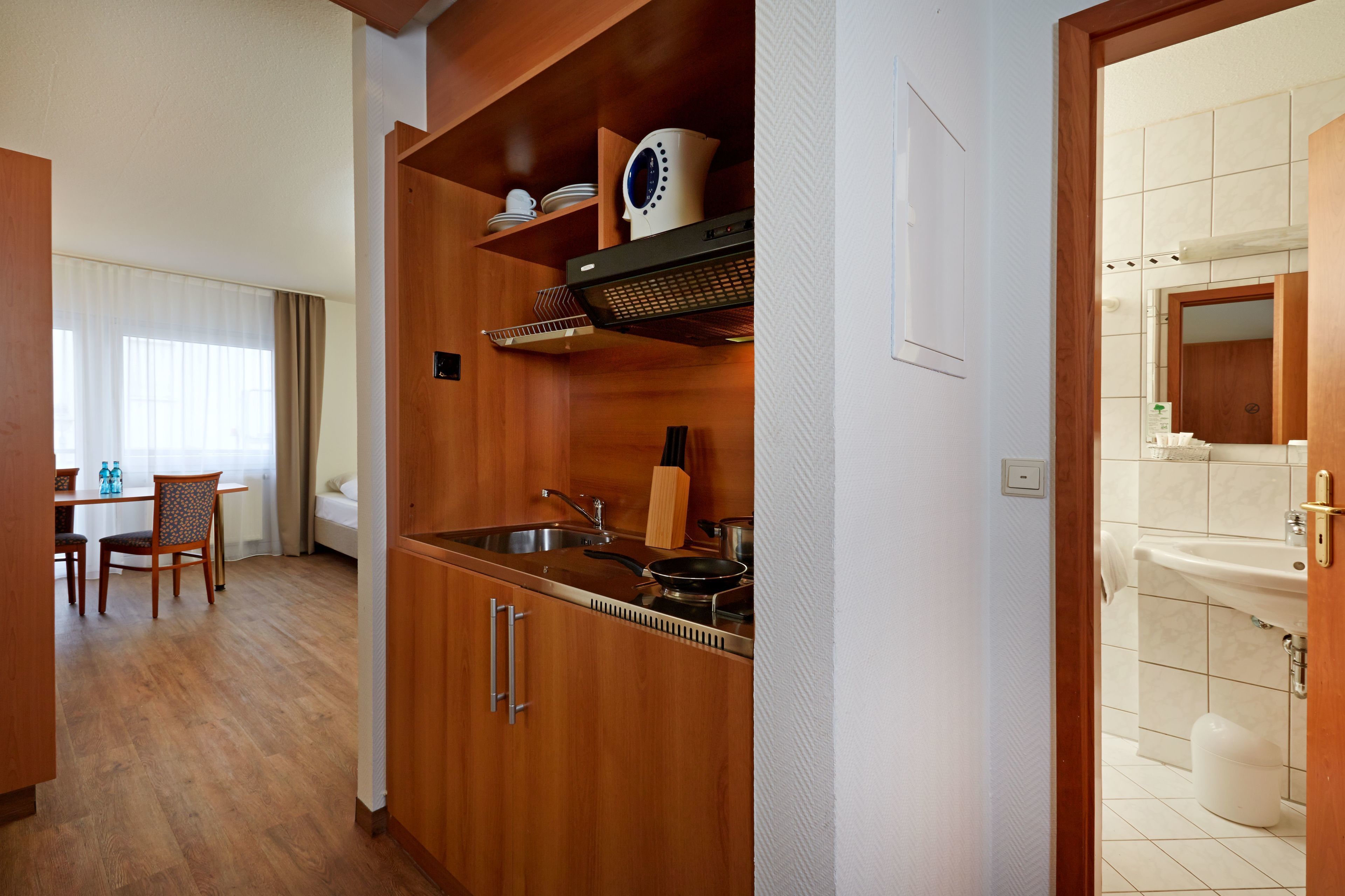 A compact kitchen with wooden cabinets, a built-in stove, and a sink. There is a dining area with a table and chairs visible in the background.