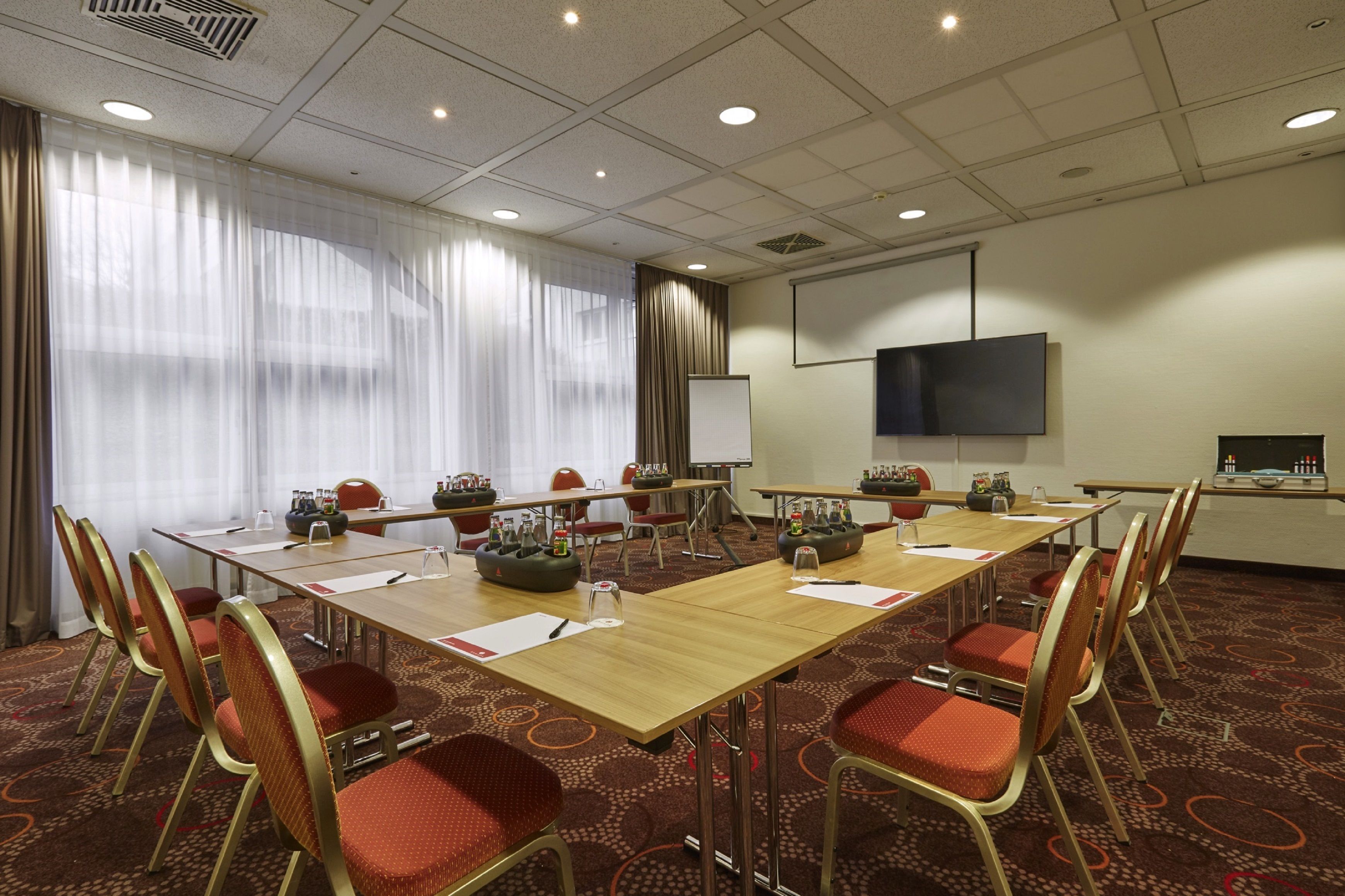 A conference room with a long table, red chairs, a projector screen, and a whiteboard.