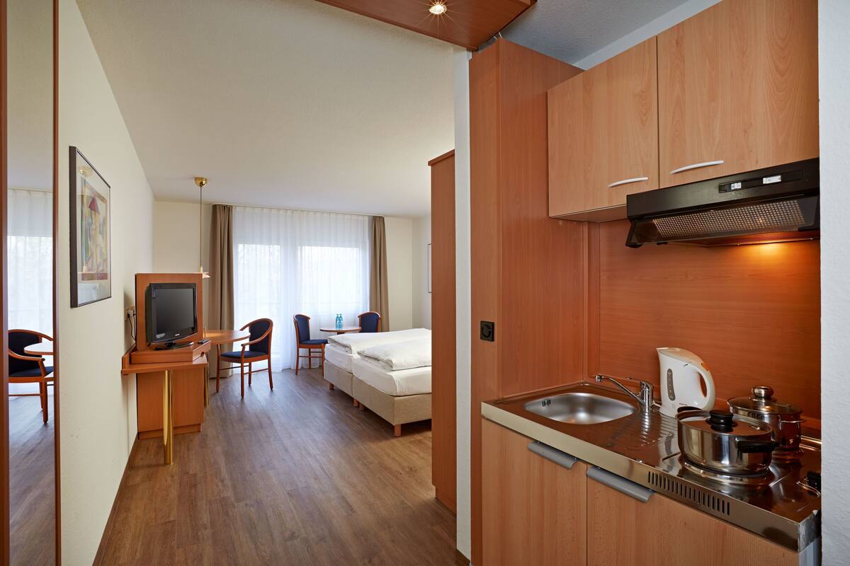 Une chambre d’hôtel compacte comprenant un coin cuisine, un lit, une télévision et un espace salon.