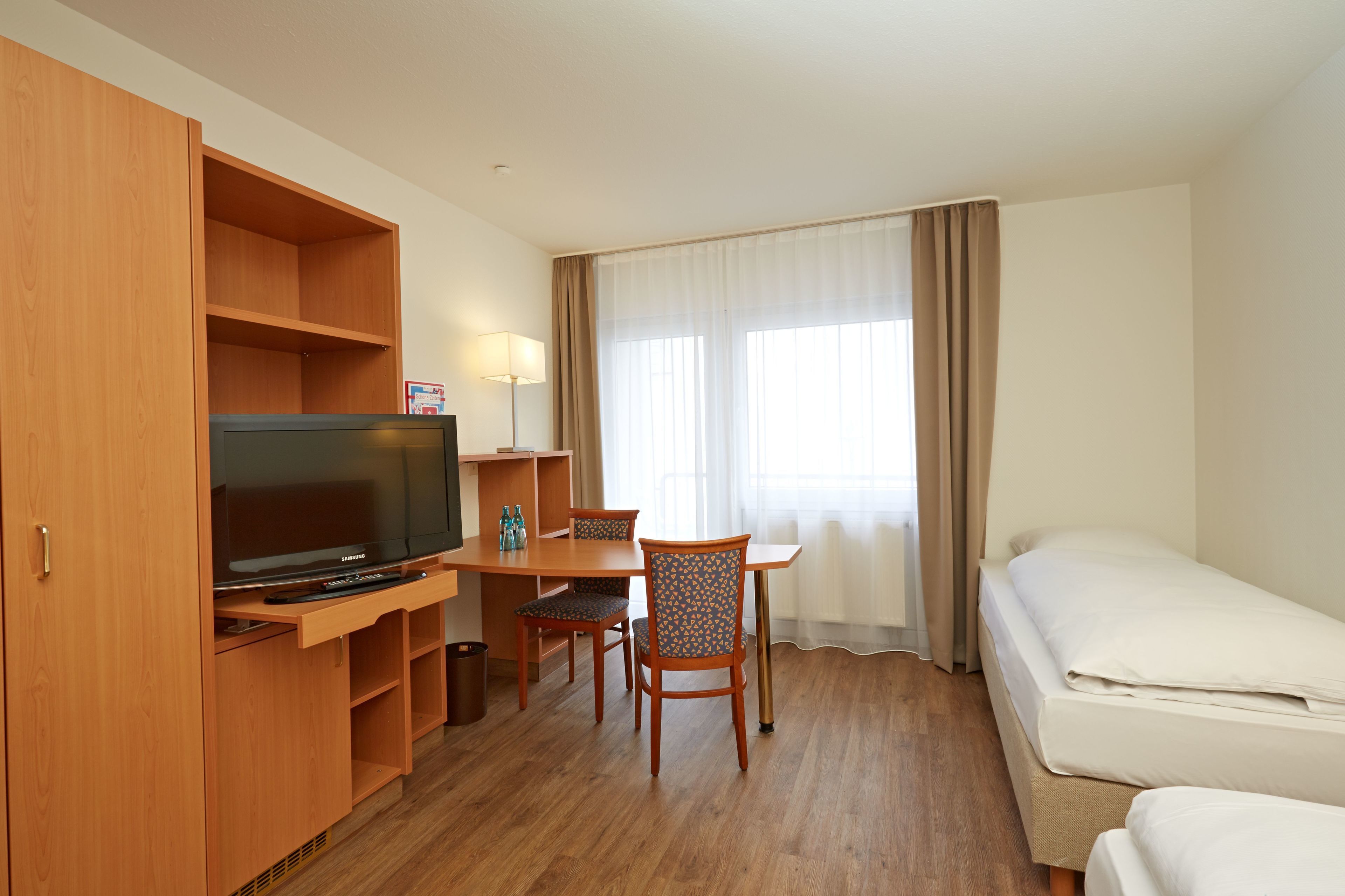 Una habitación de hotel con un escritorio de madera, un televisor, una cama y una ventana con cortinas.