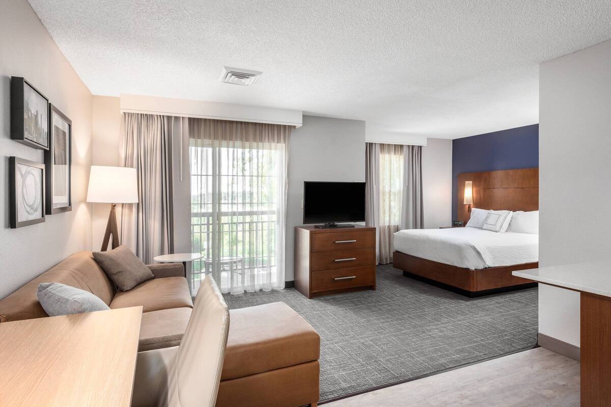 A hotel room with a sofa, a bed, a TV, a desk, and a window with curtains.
