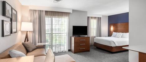 Habitación de hotel con sofá, cama, televisión, escritorio y ventana con cortinas.