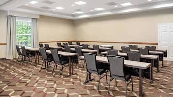 A conference room with multiple tables and chairs, carpeted floor, and a large window with curtains.