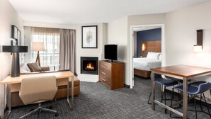 A hotel room with a desk, chair, TV, fireplace, bed, and a small dining area. - Residence Inn by Marriott Springfield (Springfield)
