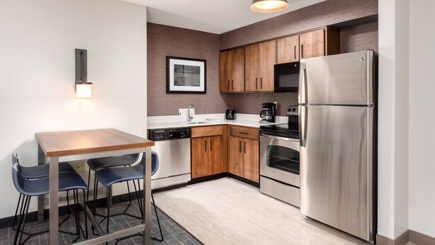 A compact kitchen with wooden cabinets, a stainless steel refrigerator, a dishwasher, and a coffee maker.