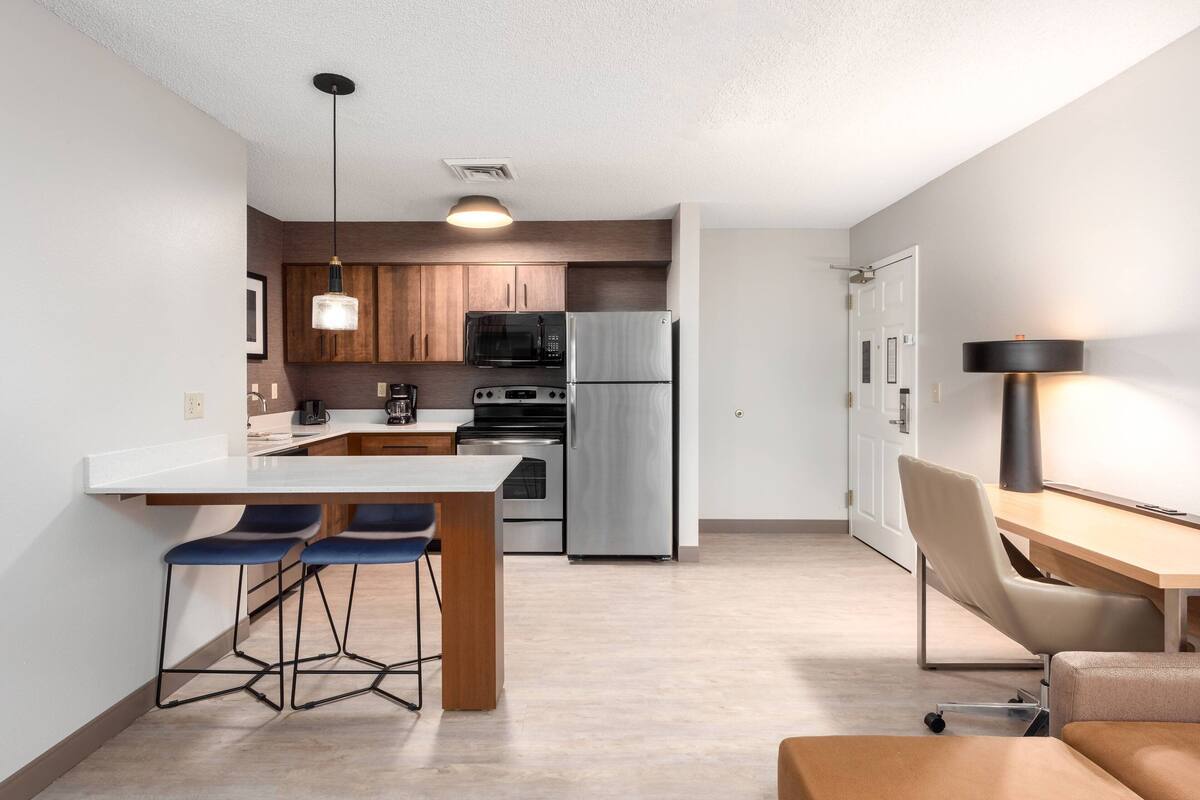 A modern kitchen with a central island, bar stools, a dining table, and a bar area.