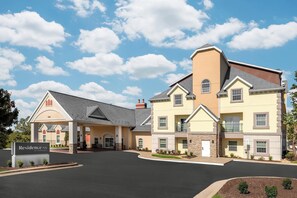 A multi-story hotel with a central entrance, a sign indicating it's a Marriott property, and a landscaped driveway.