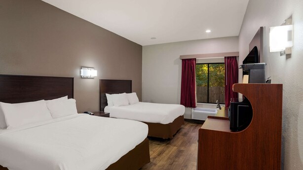 Une chambre d’hôtel avec deux lits, un bureau en bois, une télévision et une fenêtre avec des rideaux.
