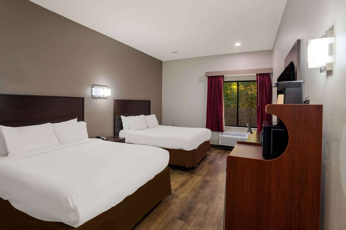 A hotel room with two beds, a wooden desk, a television, and a window with curtains.
