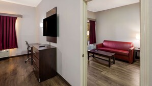 Une chambre d’hôtel moderne avec un bureau en bois, un téléviseur à écran plat, un canapé en cuir rouge et une table basse en bois.