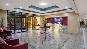 Un espace d’accueil d’hôtel doté d’une entrée avec porte vitrée, d’un comptoir de réception et d’un coin salon avec des chaises et une table.