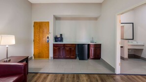 Une chambre d’hôtel compacte comprenant un coin cuisine, une porte en bois, une petite table avec une lampe et une chaise rouge.