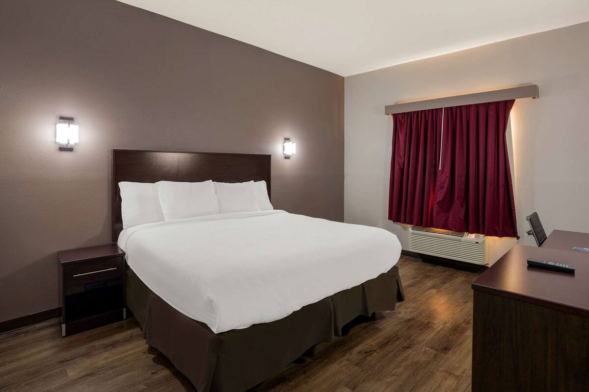 A hotel room with a large bed, bedside tables, a desk, and a window with red curtains.