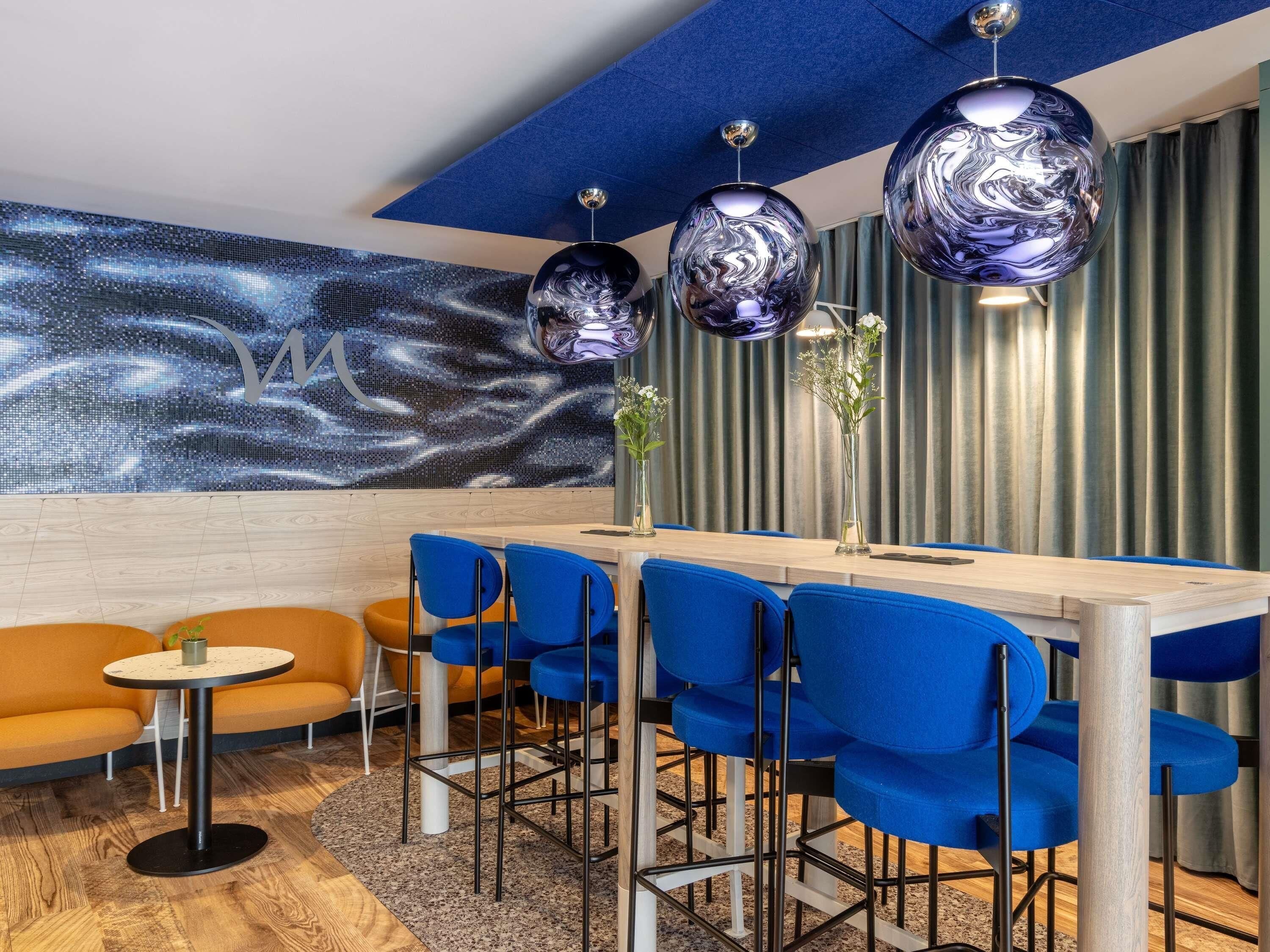 Een moderne eetruimte met een houten tafel, blauwe stoelen en een decoratieve wand met een sterrenstelsel motief.