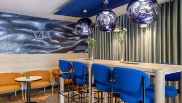 Een moderne eetruimte met een houten tafel, blauwe stoelen en een decoratieve wand met een sterrenstelsel motief.