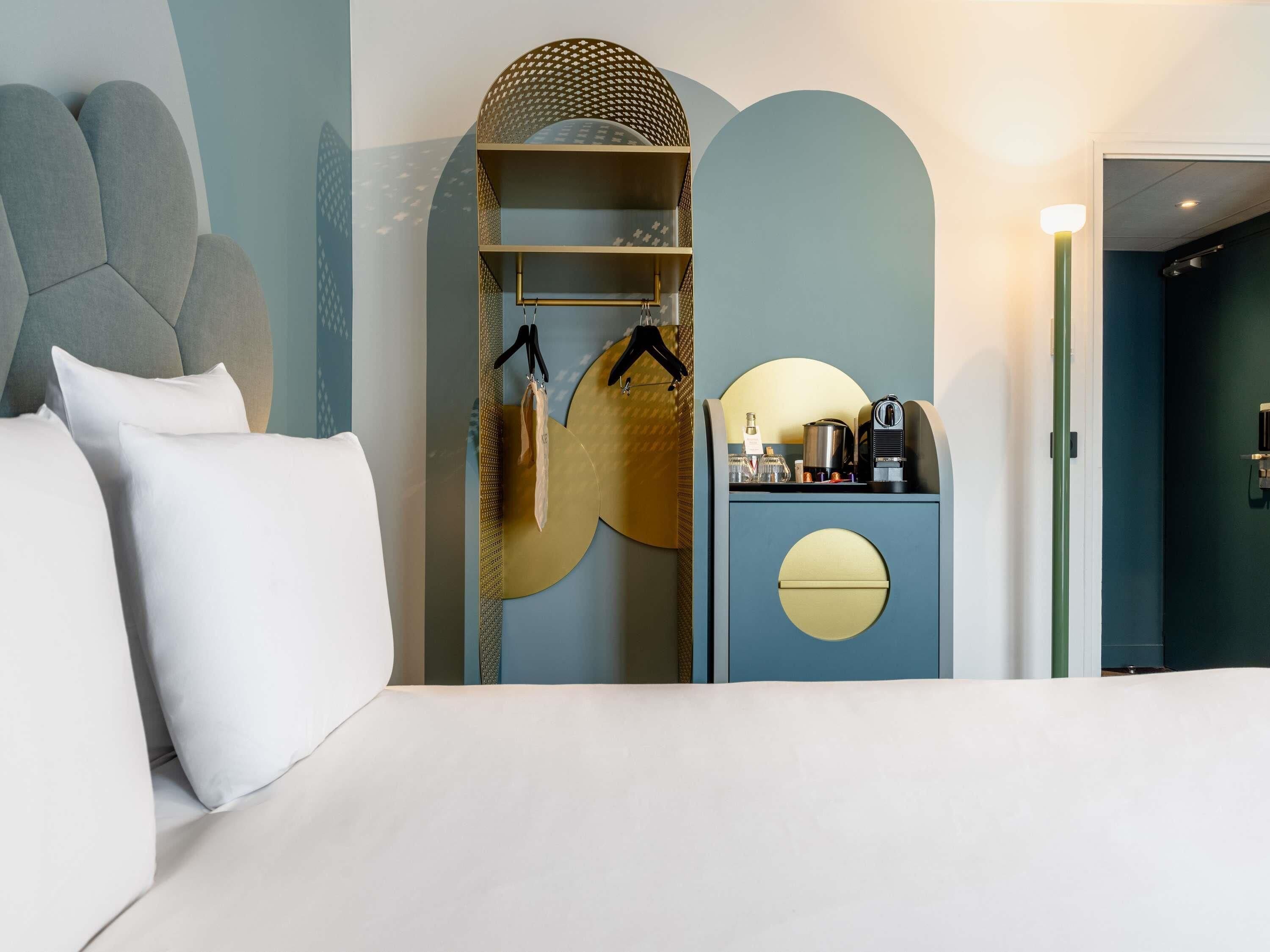 A modern hotel room with a bed, a wardrobe, and a small kitchenette.