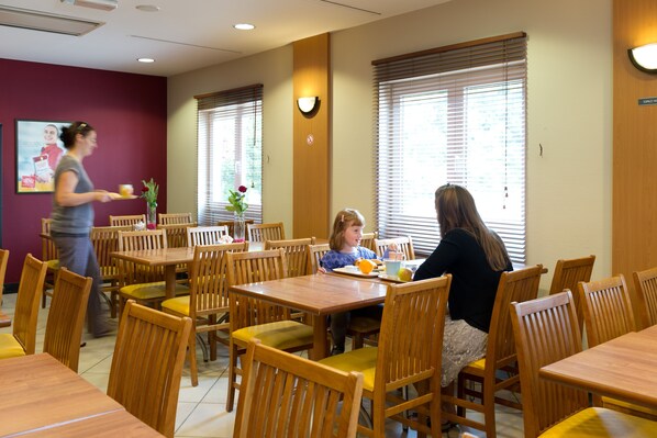 A dining area with wooden tables and chairs, a woman serving food, and a child seated at a table. - ibis Liège Seraing (Seraing)