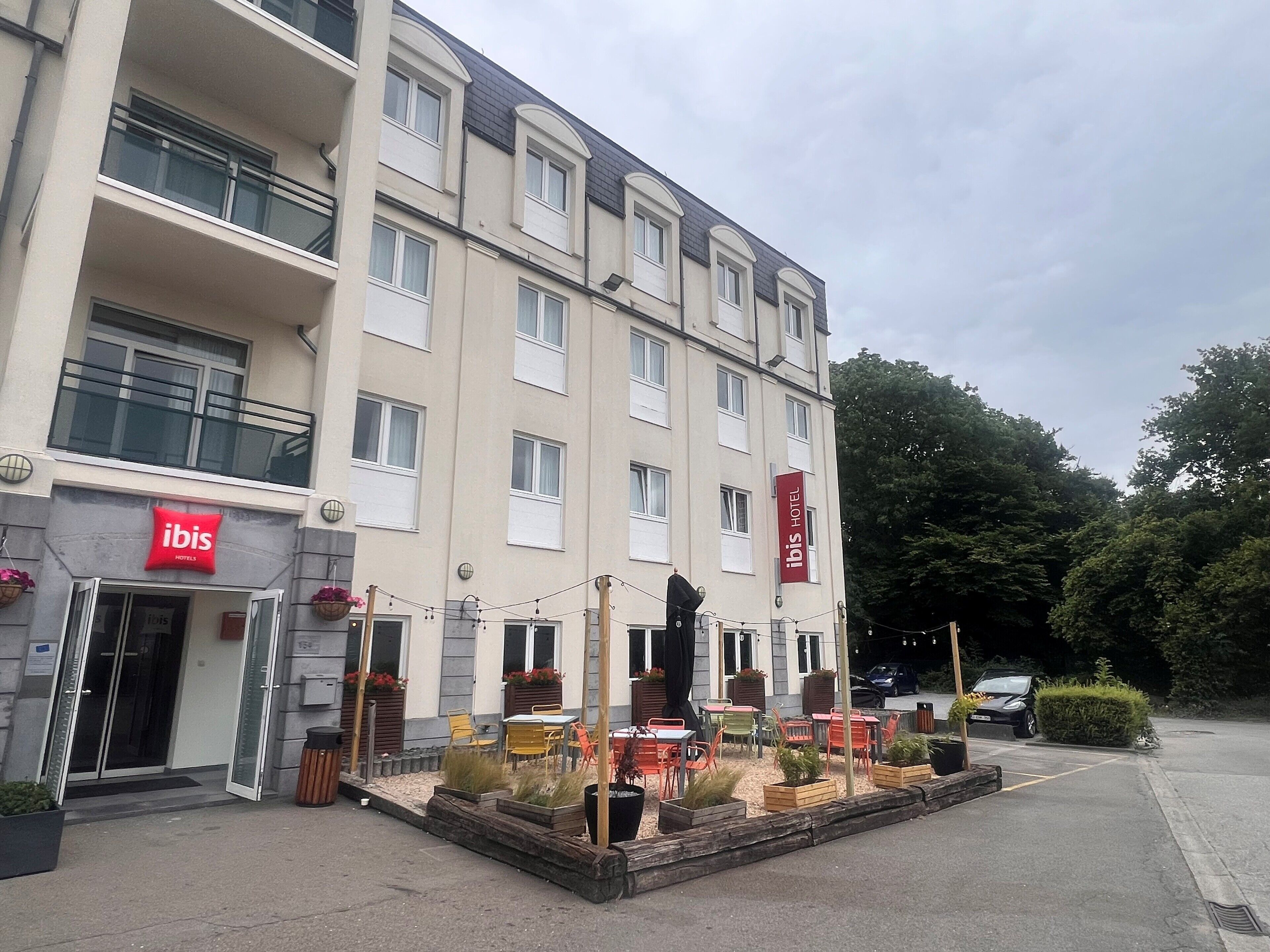 Un hôtel avec une enseigne rouge et blanche, des tables et des chaises disposées à l’extérieur, et un balcon.