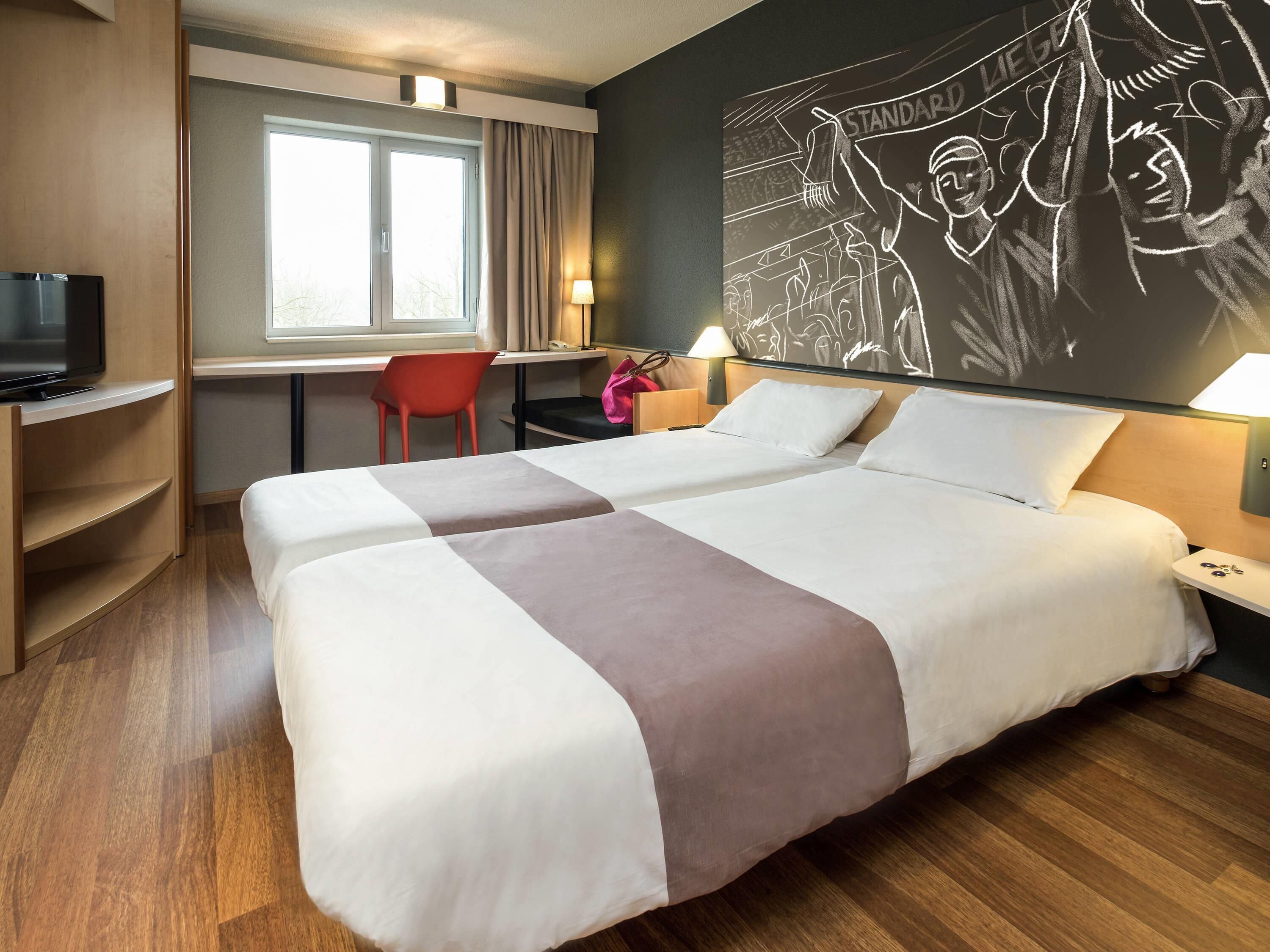 A hotel room with two beds, a desk, a chair, a TV, and a wall mural.