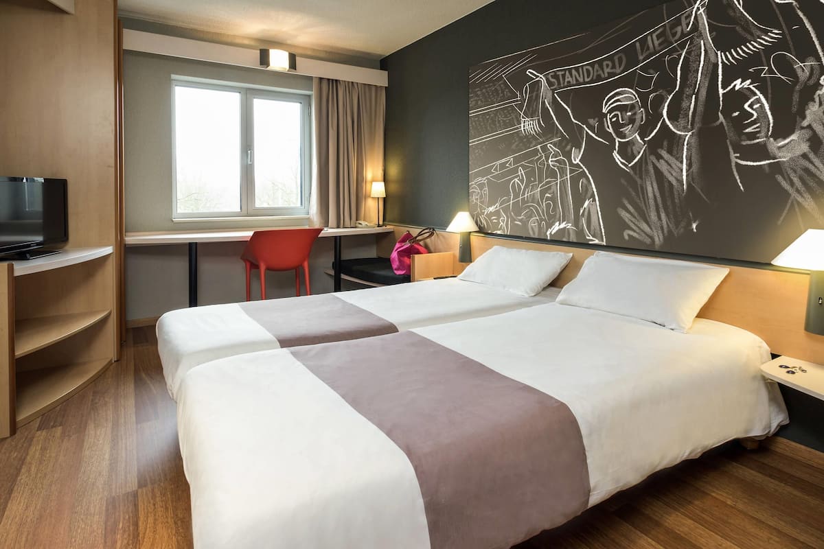 A hotel room with two beds, a desk, a chair, a TV, and a wall mural.