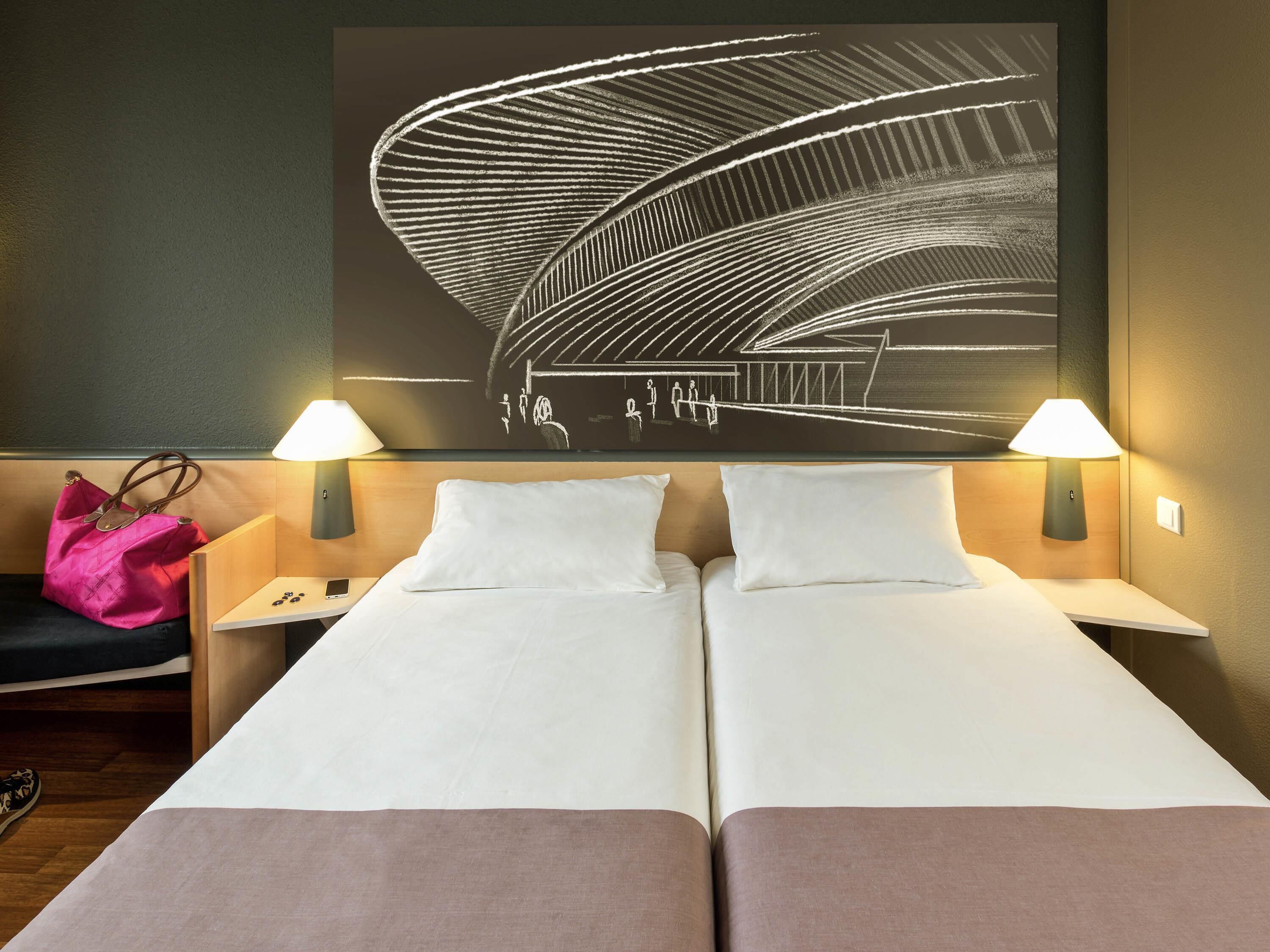 A hotel room with two beds, a large abstract artwork on the wall, two bedside lamps, and a pink bag on the left side.