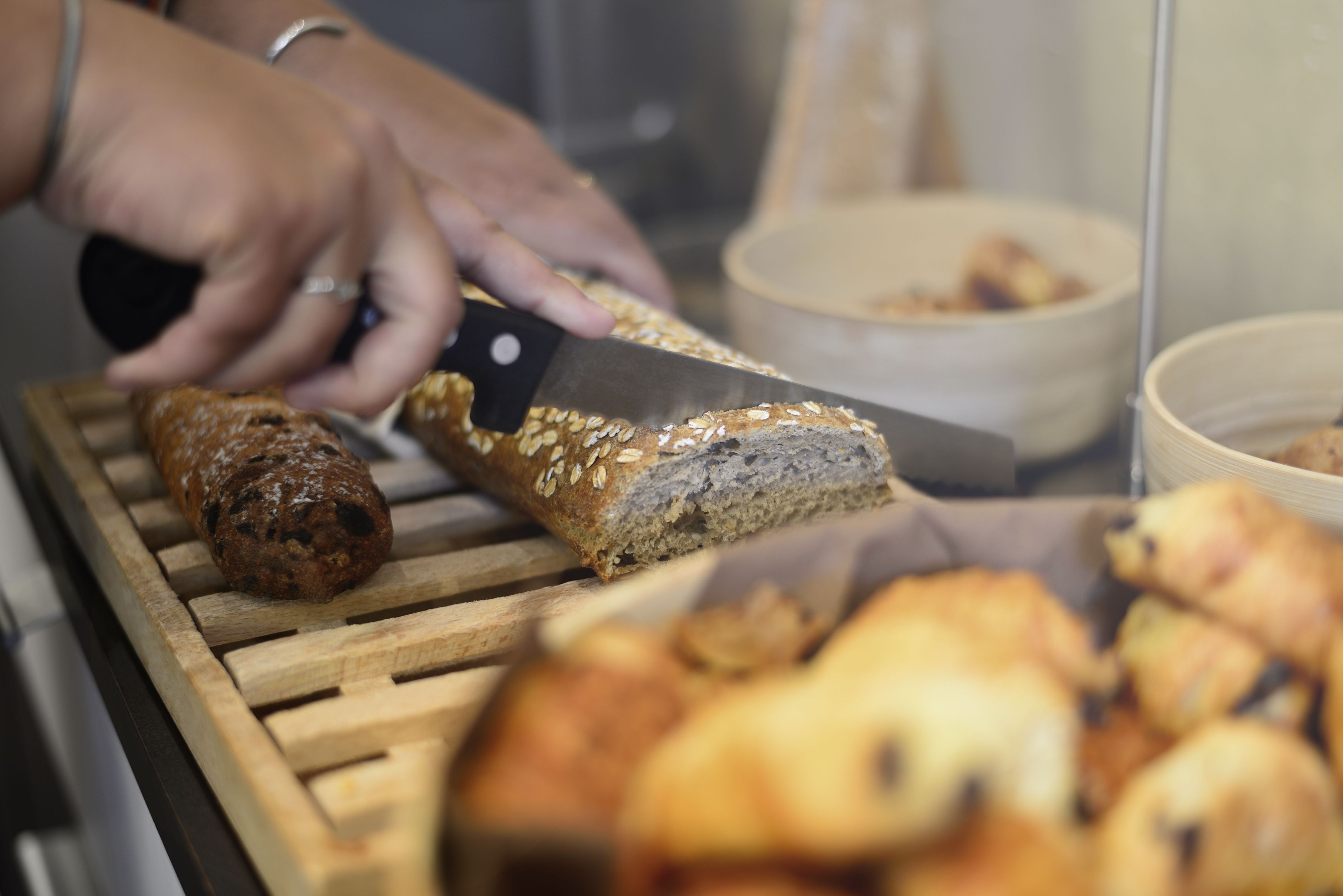 A person slicing a loaf of bread with a knife on a wooden cutting board.