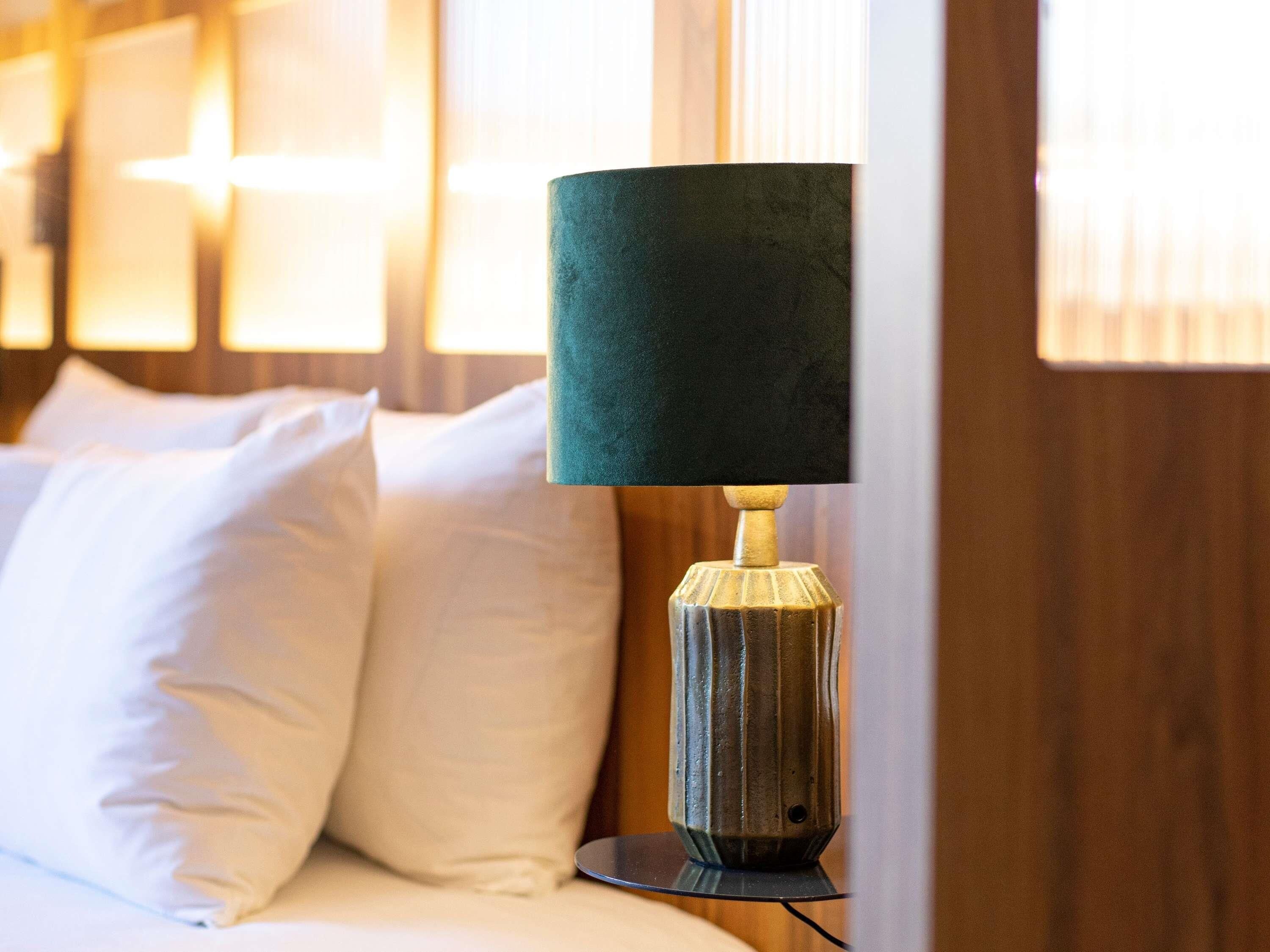 A bed with white pillows and a lamp with a textured shade on a bedside table.