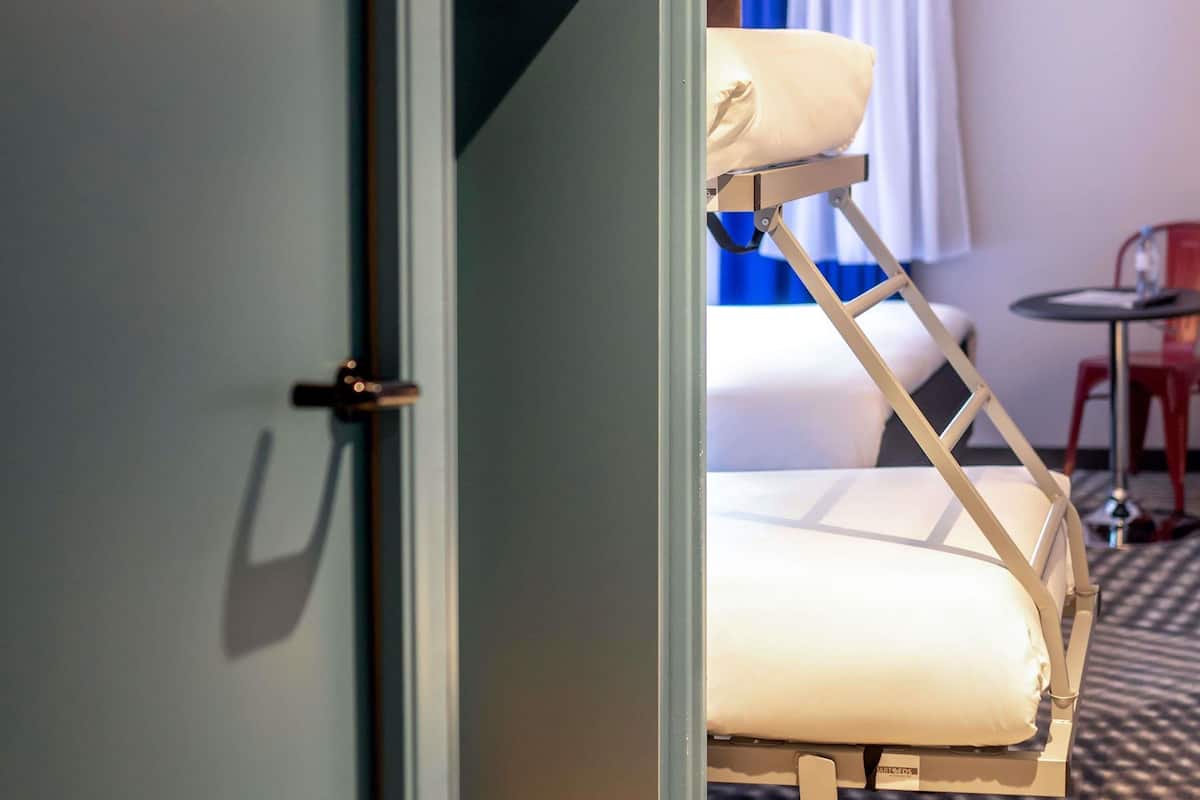 Une chambre d’hôtel avec un lit, une chaise, une petite table et une porte.