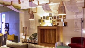 A modern hotel lobby with a wooden reception desk, a sofa, a chair, and pendant lighting. - ibis Styles Saint Étienne Gare Châteaucreux (Saint-Etienne)
