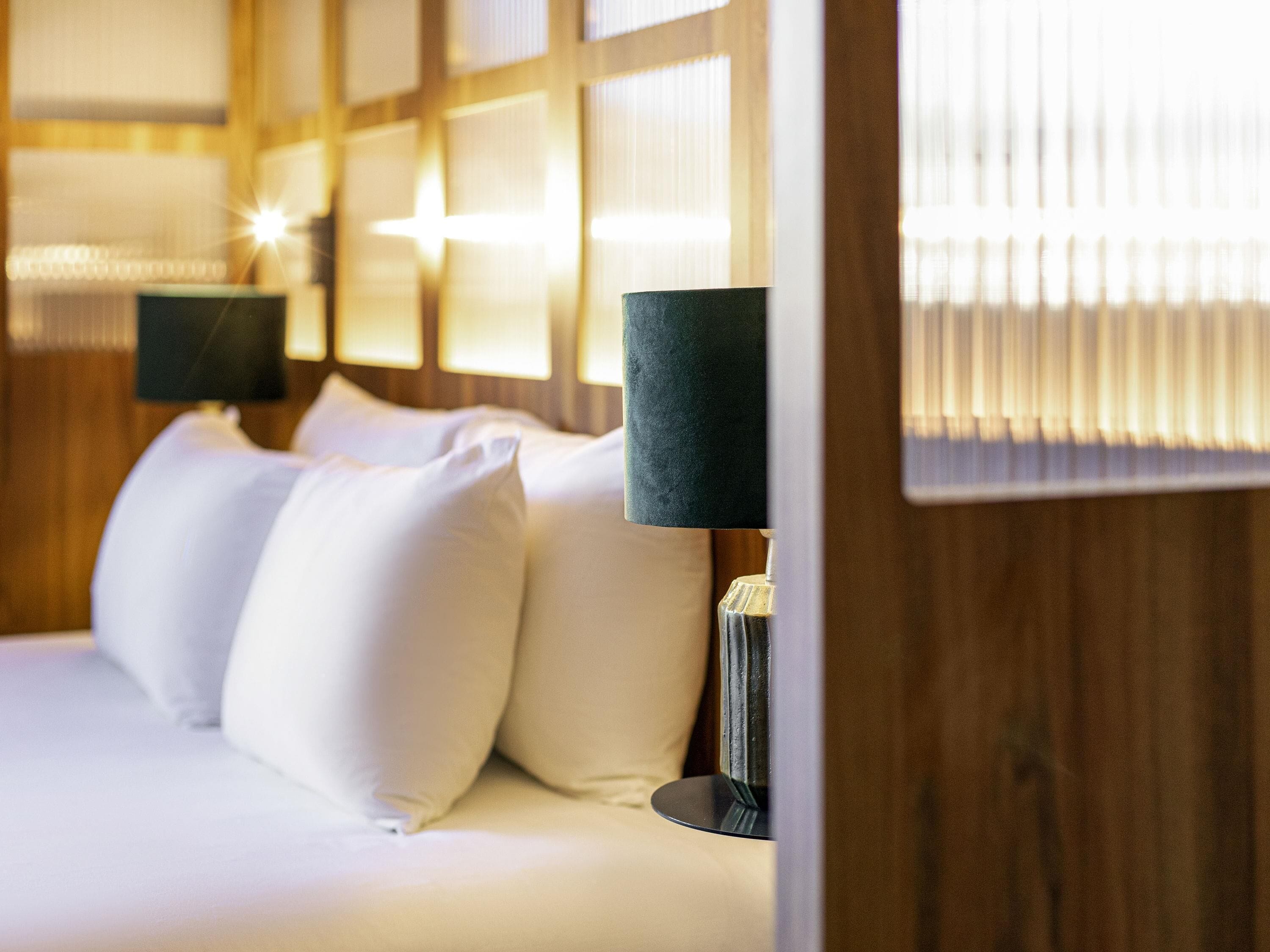 A neatly made bed with white linens and two lamps with dark shades on either side.