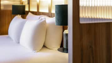 A neatly made bed with white linens and two lamps with dark shades on either side.