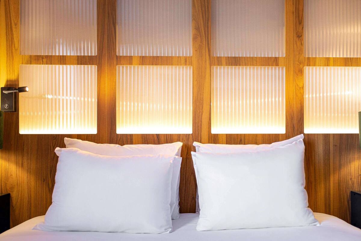 A hotel room with a wooden wall, two white pillows, and a bed.