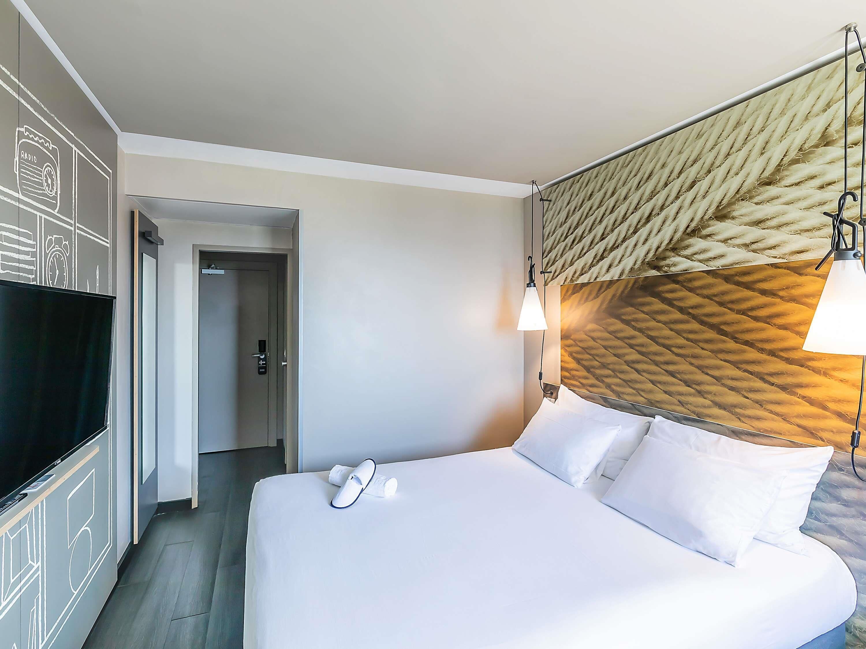 Una camera d'albergo con un letto, una televisione, una porta e un muro con motivo decorativo.