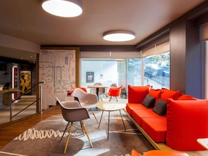 Un interno moderno con un divano rosso, una scrivania in legno all'accoglienza e un'ampia finestra con vista sulla strada.
