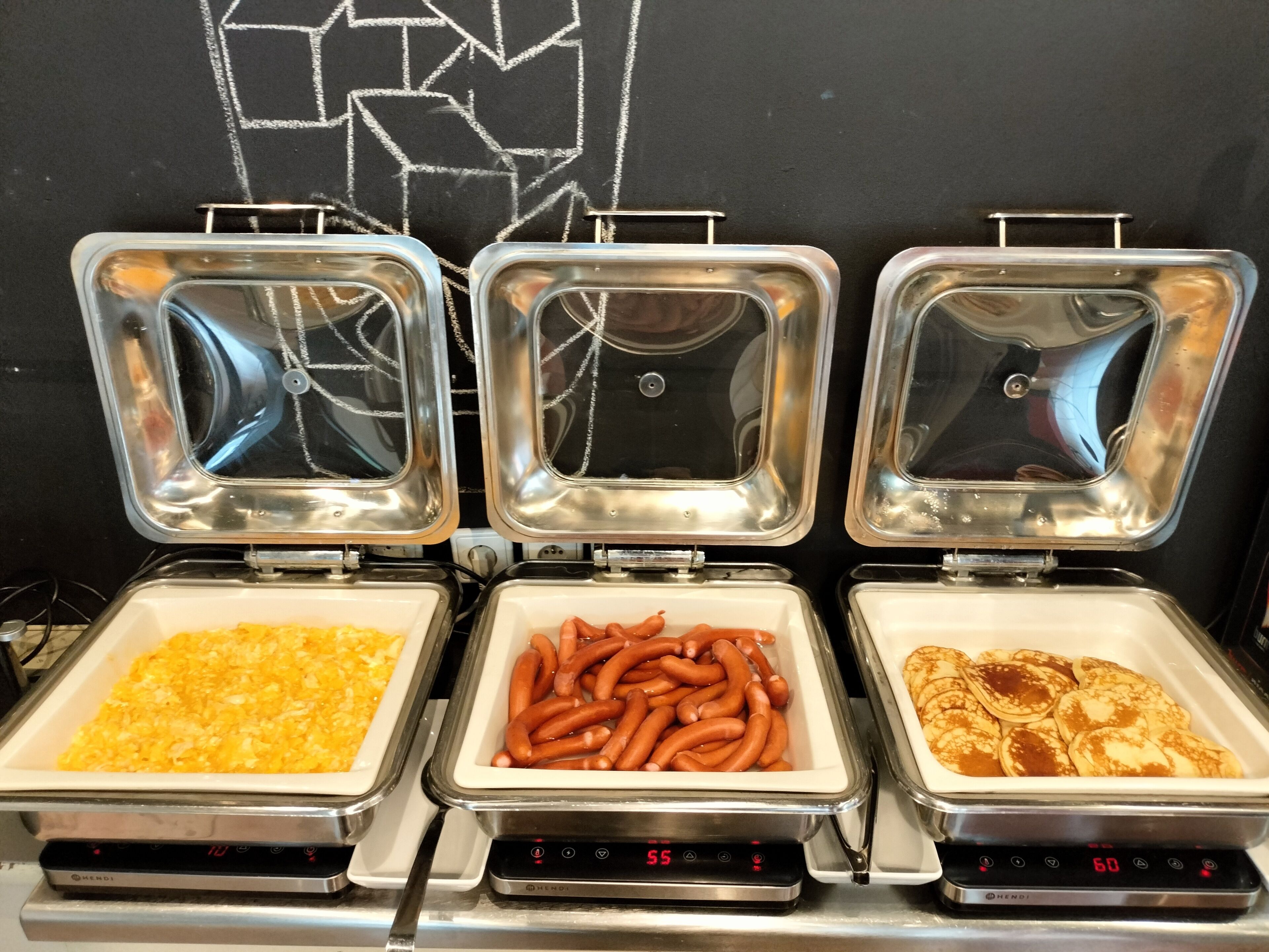 Three buffet trays with different food items: scrambled eggs, sausages, and pancakes.
