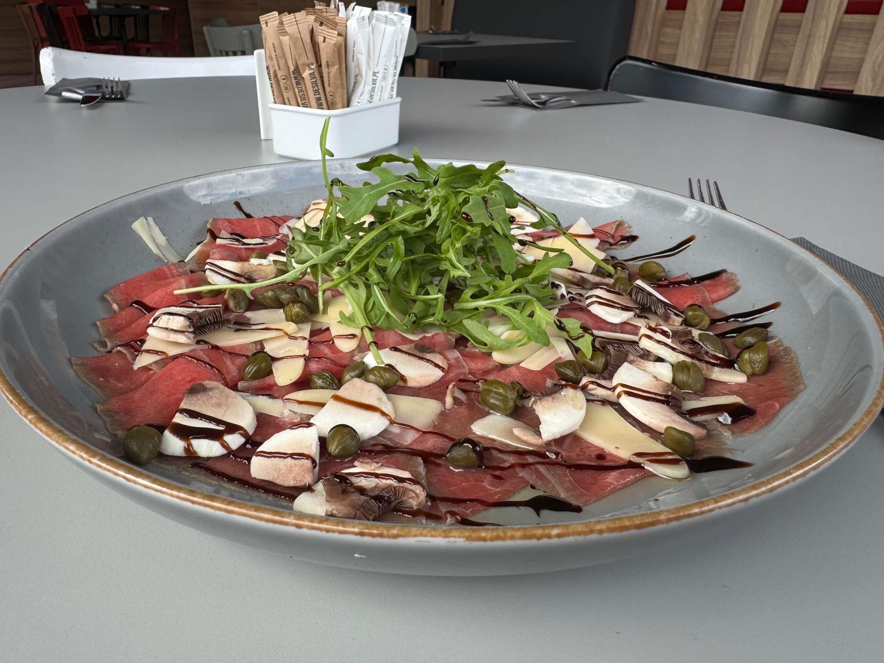 A plate of sliced meats, cheese, and greens on a table.