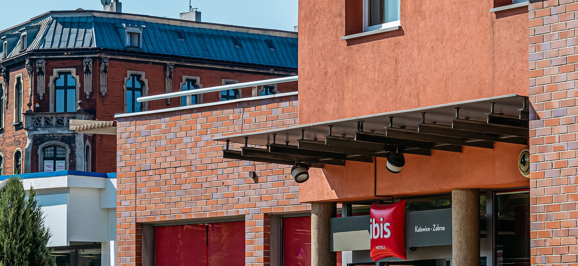 A hotel with a red facade, a sign for 'Hotel ibis Katowice - Zabrze', and a blue building in the background.