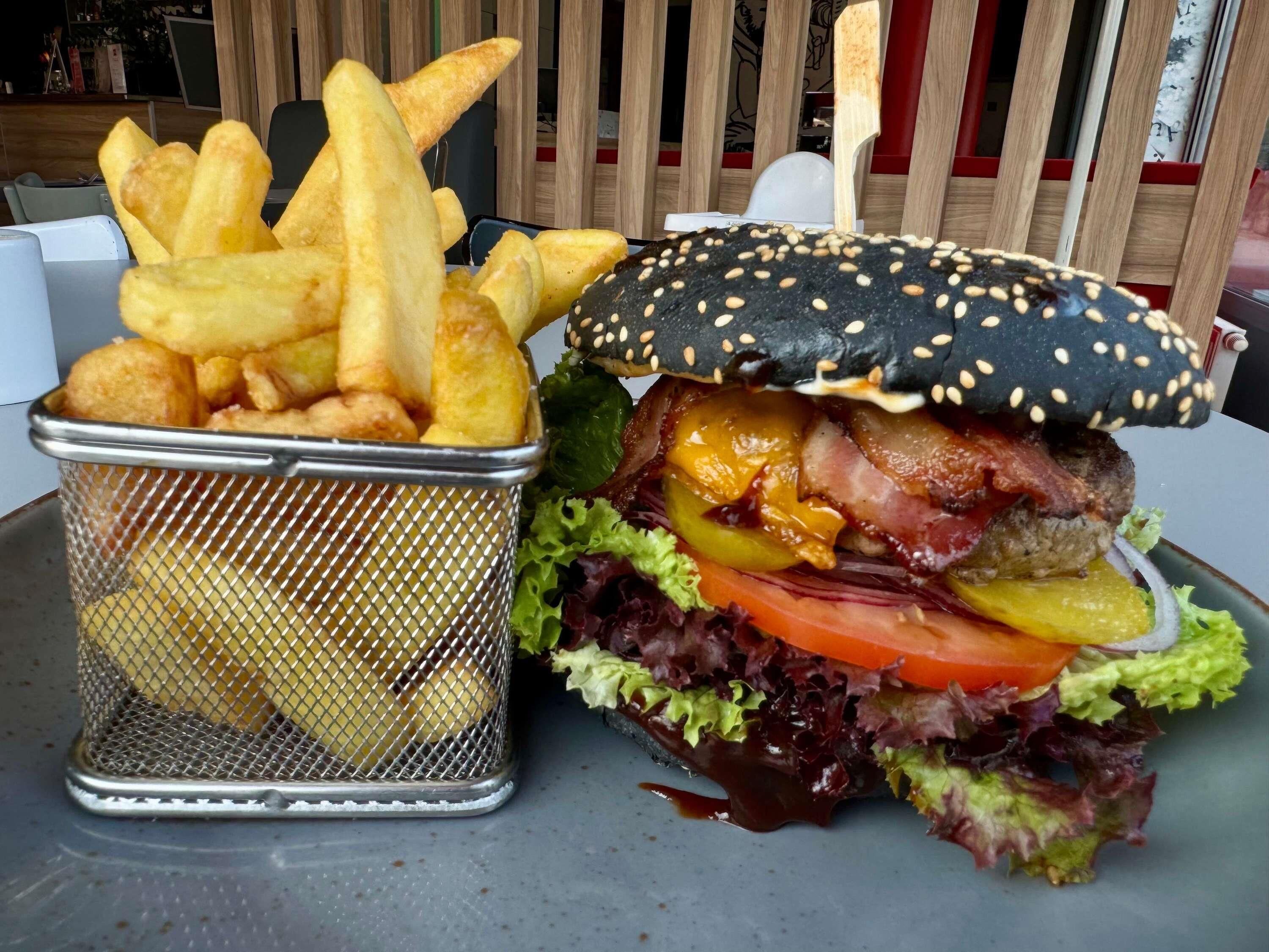 Una hamburguesa con lechuga, tomate y queso, junto con una cesta de papas fritas.