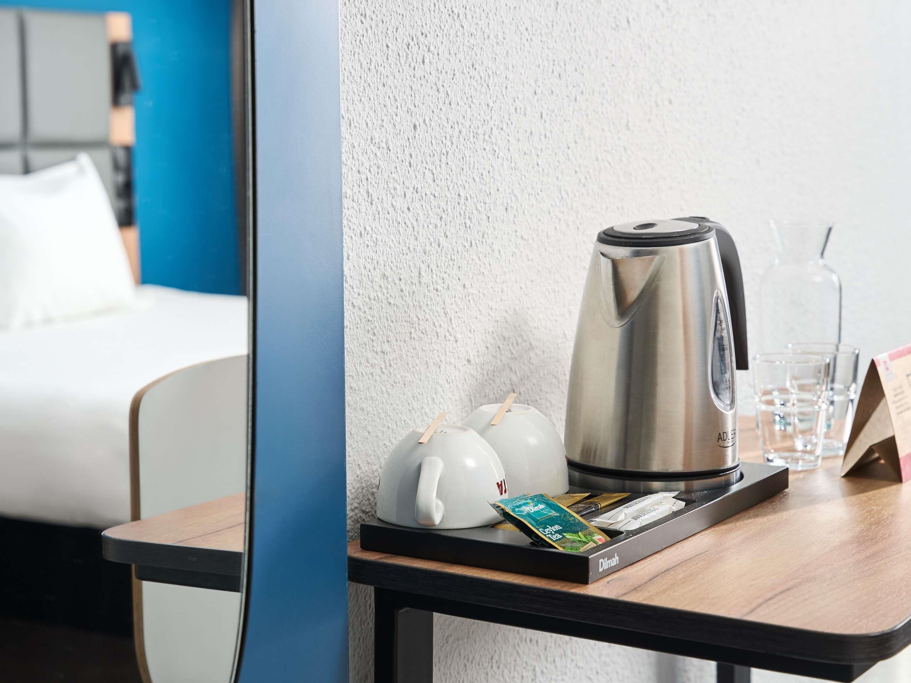 Habitació d'hotel amb un llit, una cafetera, una safata amb sobres de te i un got d'aigua.