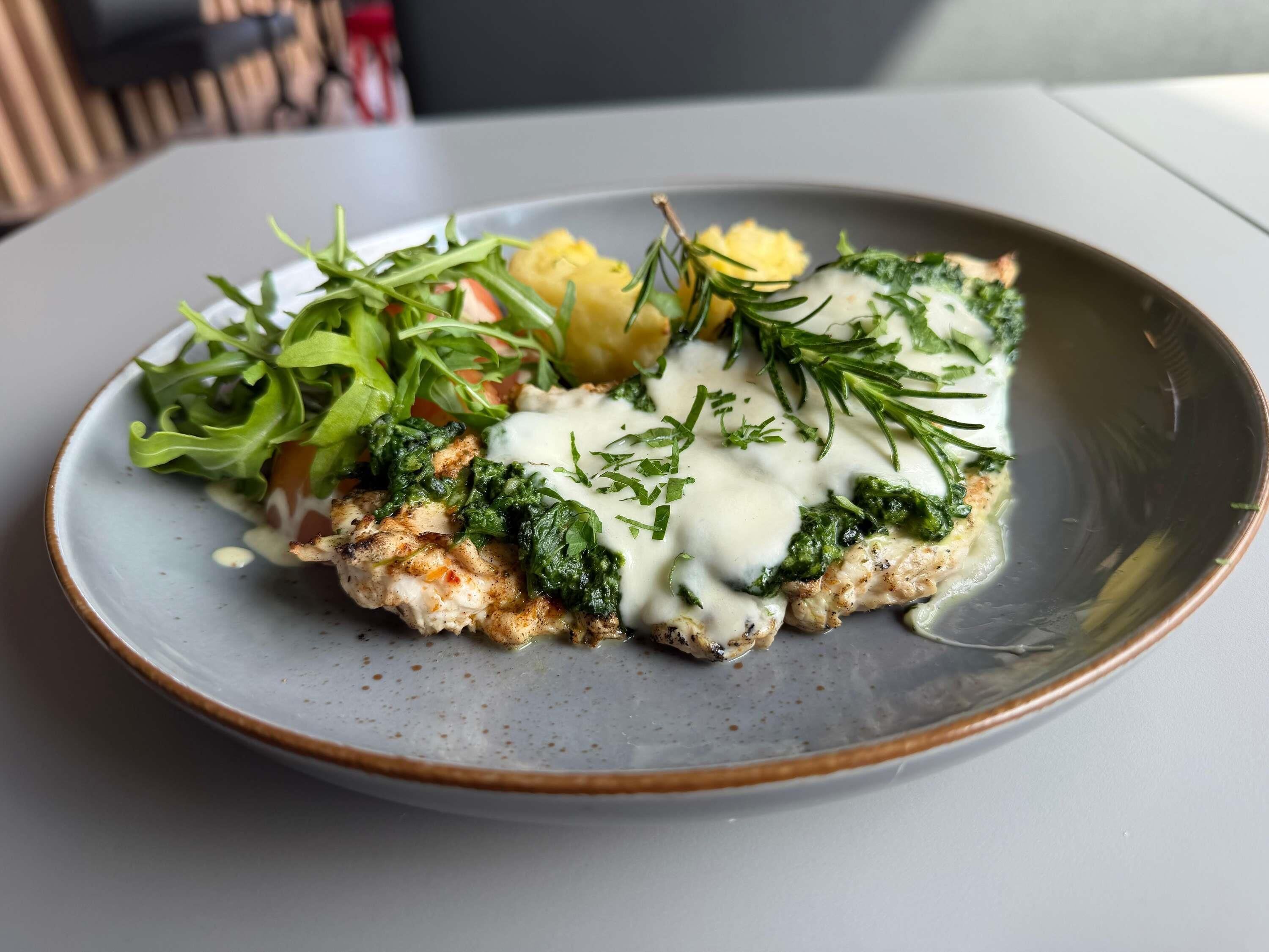 A plate of food with a creamy sauce, greens, and a side of potatoes.