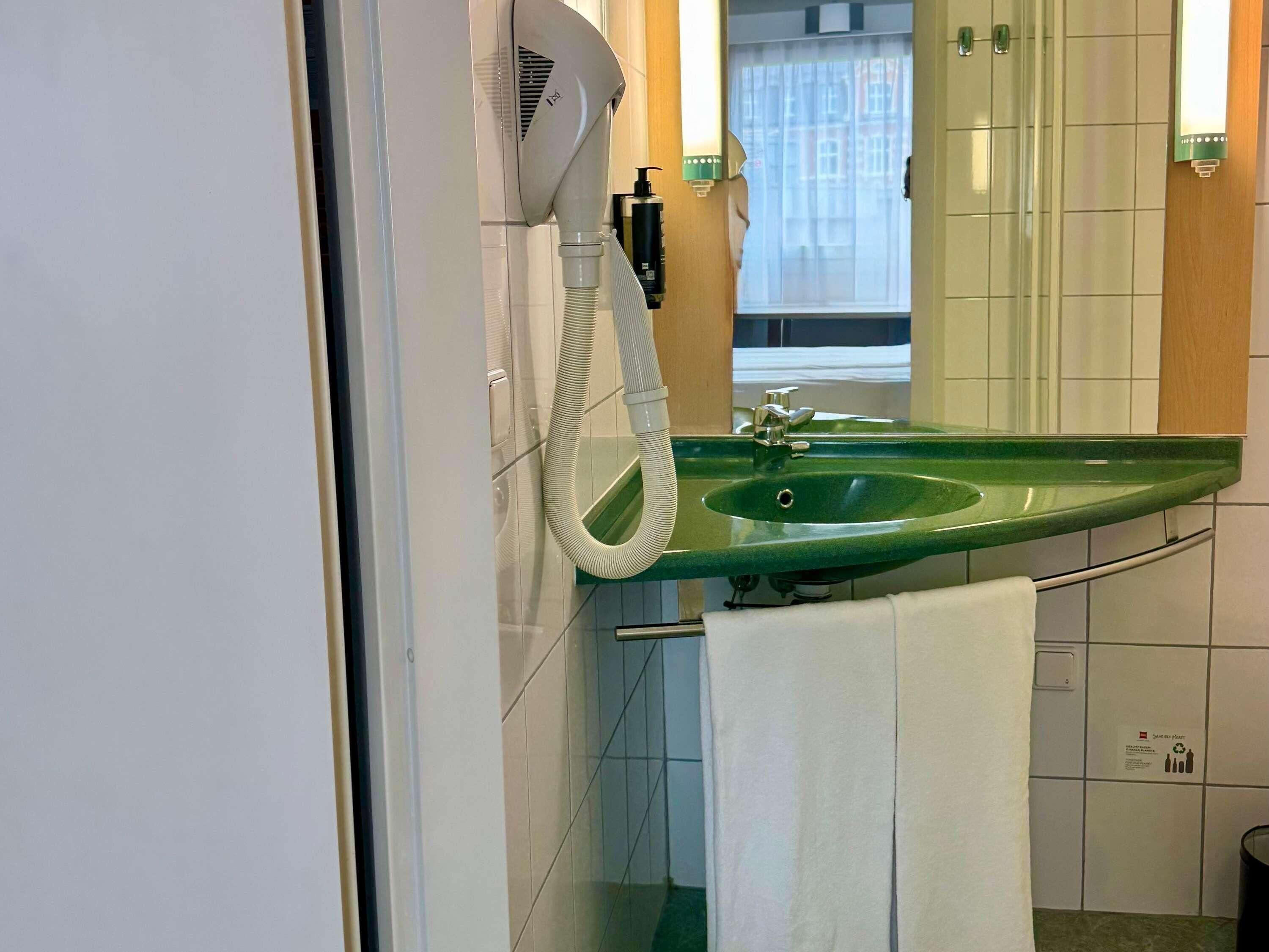 A bathroom with a green sink, a hairdryer, a mirror, and a towel hanging on the wall.